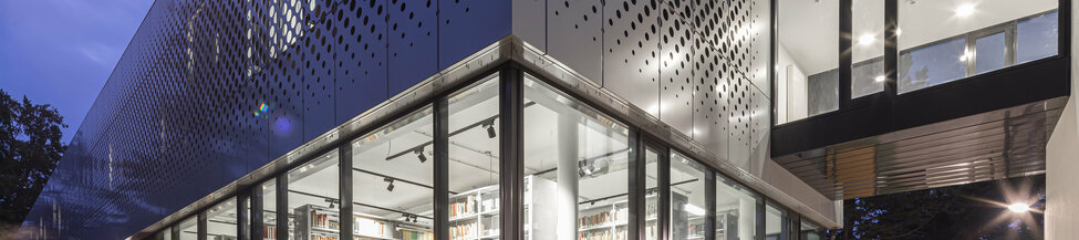 Außenansicht der innen beleuchteten Institutsbibliothek bei Nacht